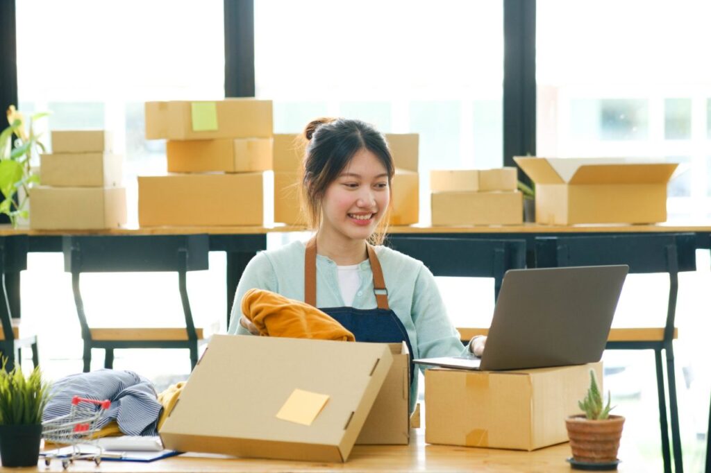 Design Hub 360 Custom T-Shirts & Apparel Printing 2 asian female clothes shop owner folding a t shirt and packing in a cardboard parcel box