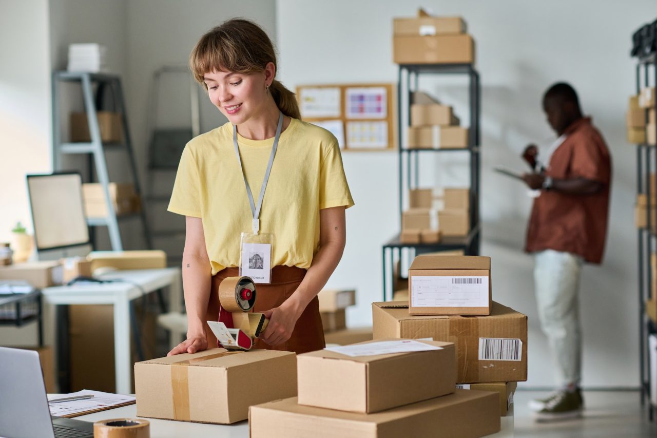 Design Hub 360 Creative Company 9 young smiling woman in yellow t shirt sealing cardboard box with cellotape